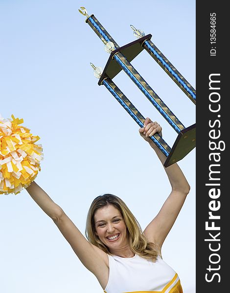 Smiling Cheerleader holding trophy, (portrait), (low angle view)