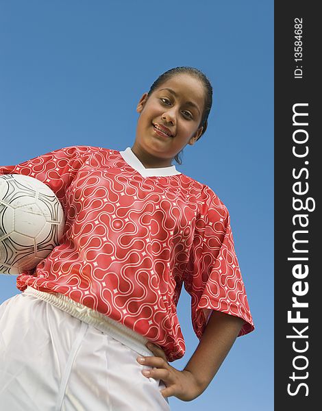 Girl (13-17) in soccer kit holding ball, portrait, low angle view