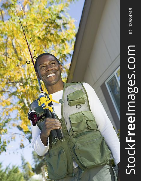 Man holding fishing rod in font of house, smiling, (low angle view)