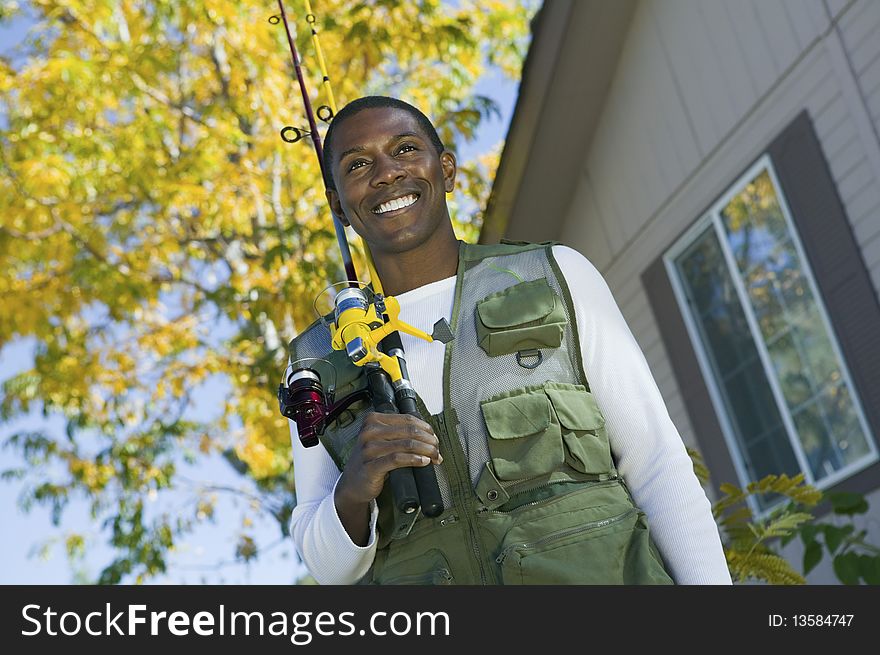 Man Holding Fishing Rod In Front Of House