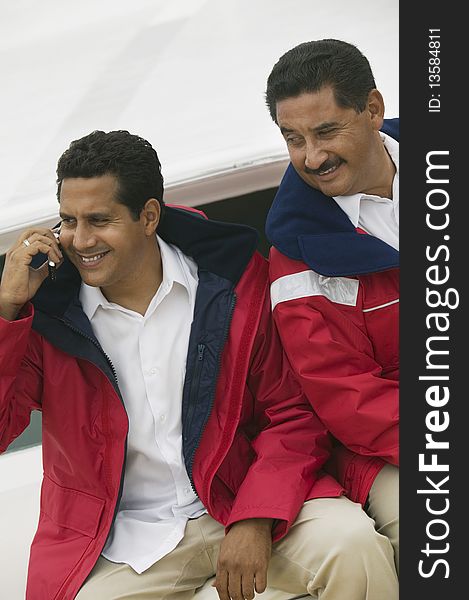 Two men relaxing on yacht, one man using mobile phone