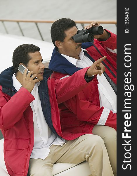 Two men relaxing on yacht, looking through binoculars and talking on mobile phone. Two men relaxing on yacht, looking through binoculars and talking on mobile phone