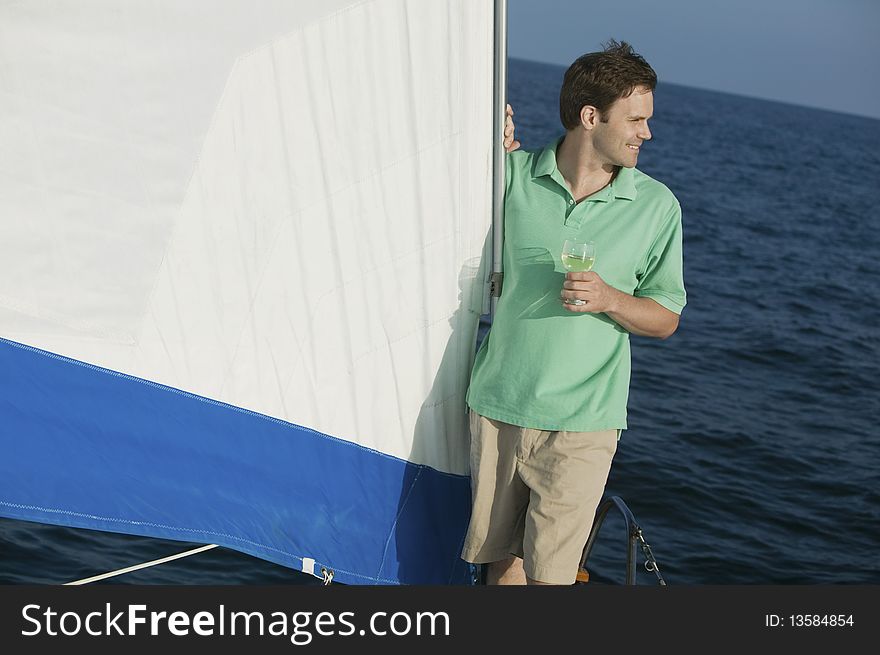 Man standing on sailboat, holding glass of white wine. Man standing on sailboat, holding glass of white wine