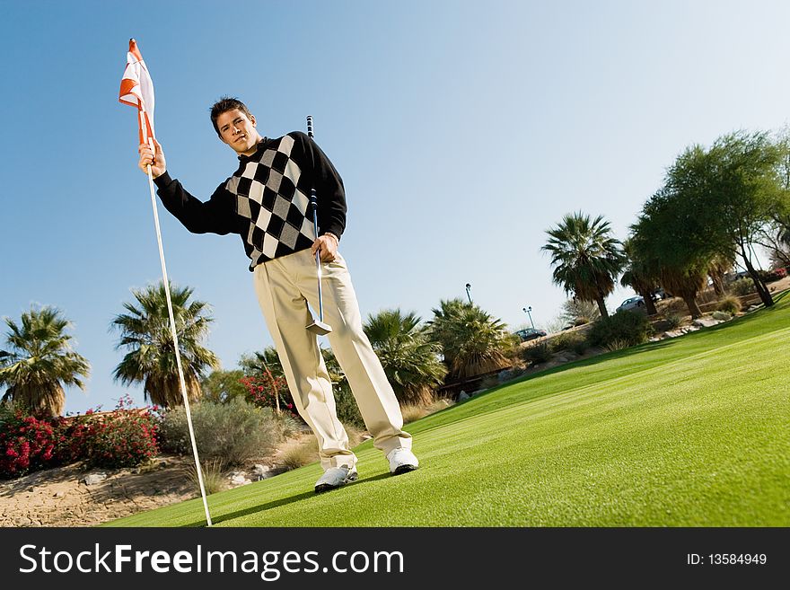 Golfer holding flag on putting green, (low angle view)