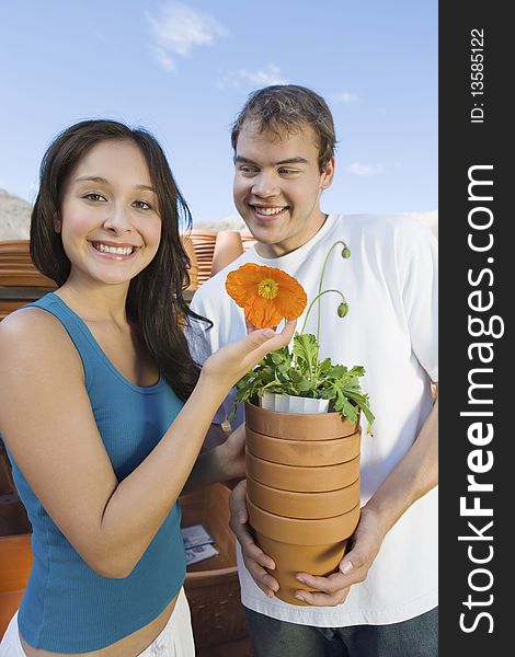 Young couple holding flower pots in outdoors garden centre, (portrait)