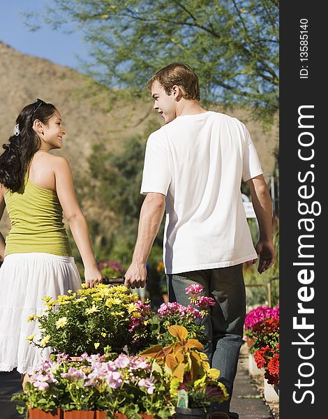 Young Couple Pulling Cart With Potted Flowers