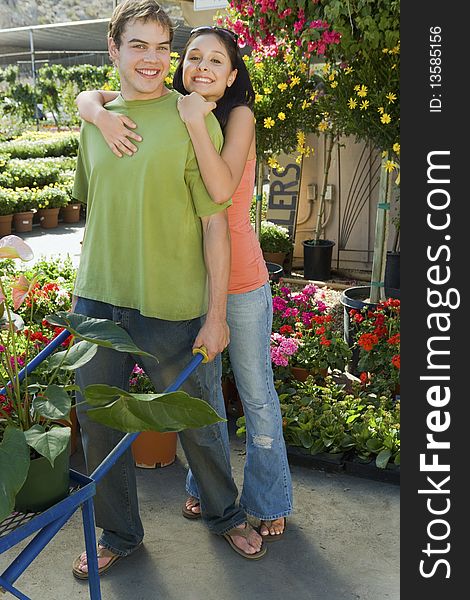 Woman embracing man with pushcart in garden centre, (portrait)