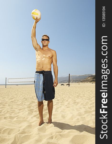 Young man in shorts standing on beach, holding volleyball above head. Young man in shorts standing on beach, holding volleyball above head