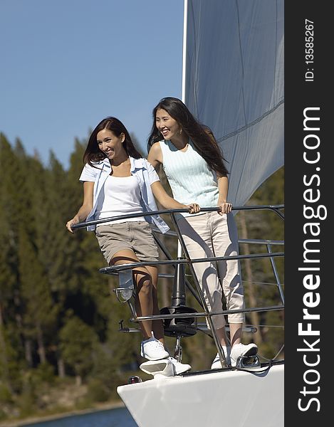 Two prettyyoung women standing on bow of sailboat