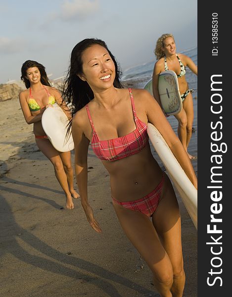 Three female surfers carrying surfboards, walking on beach