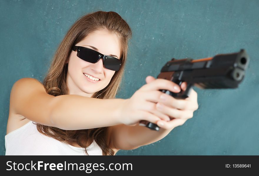 Long-haired girl in sunglasses aiming a black gun. Focus on gun only. Long-haired girl in sunglasses aiming a black gun. Focus on gun only