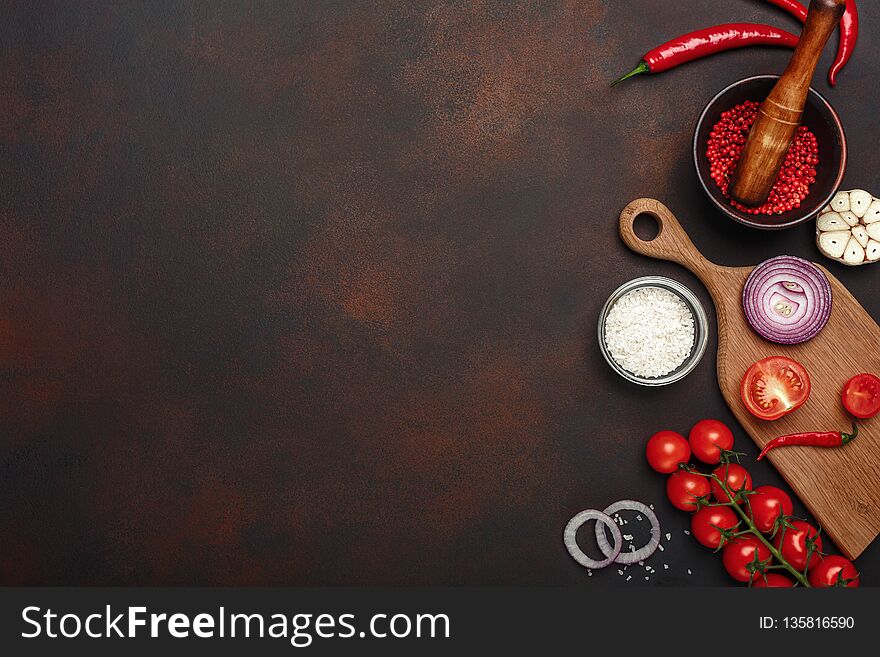 Set of products on cutting board from cherry tomatoes, rosemary, garlic, red pepper, onion, salt and spice mortar on rusty brown background. Top view with space for your text
