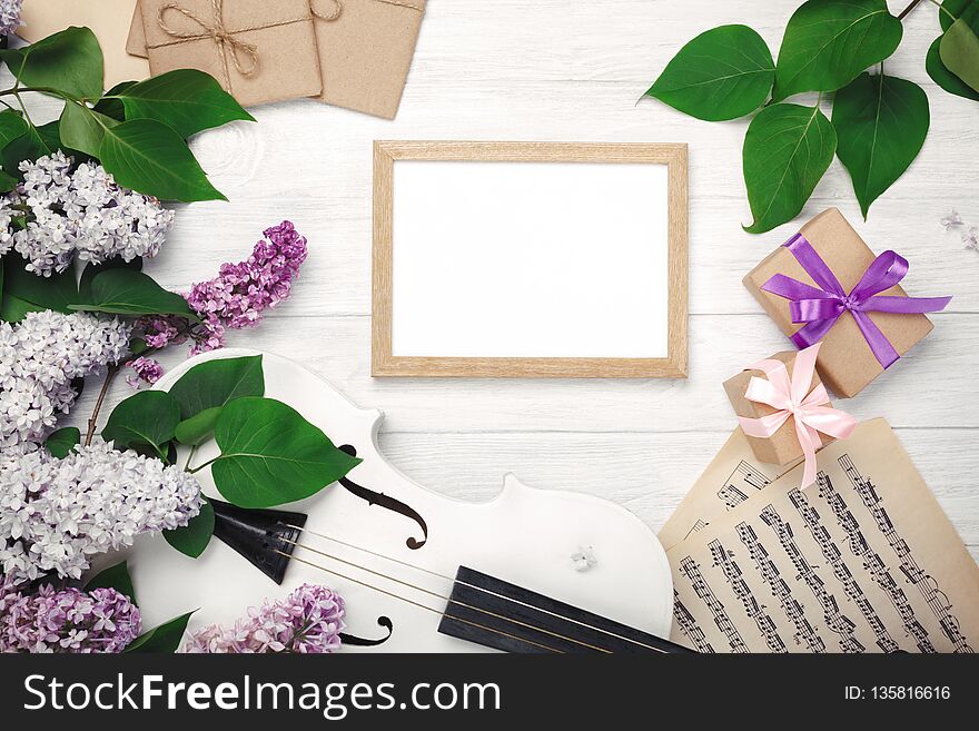 A bouquet of lilacs with violin, chalk board, gift box and music sheet on a white wooden table. Top wiev with space for your text