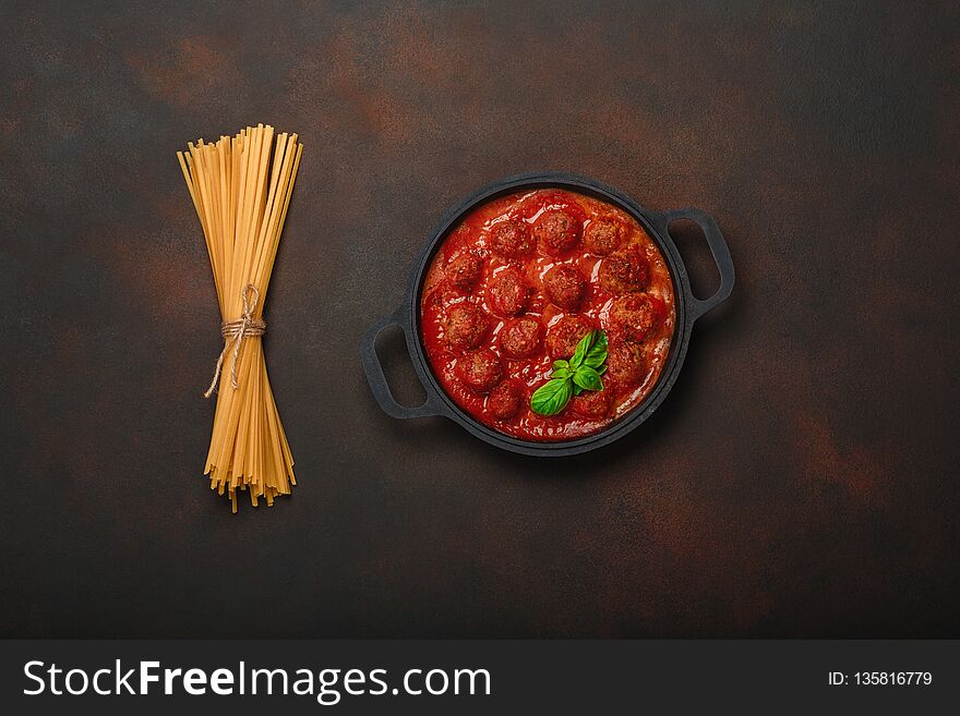Meatballs in tomato sauce with spices, pasta and basil in a frying pan on rusty brown background. Top view.
