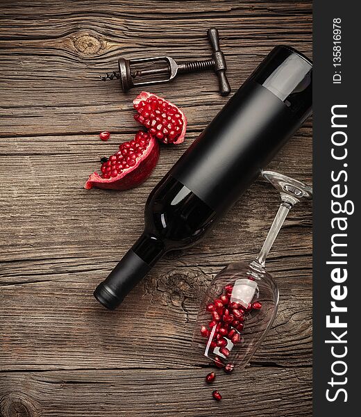 Ripe pomegranate fruit with a glass of wine, a bottle and a corkscrew on a wooden background