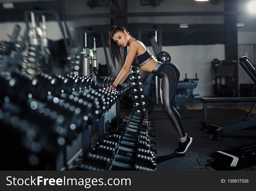 Slim, bodybuilder girl, lifts heavy dumbbell standing in front of the mirror while training in the gym. Sports concept, fat