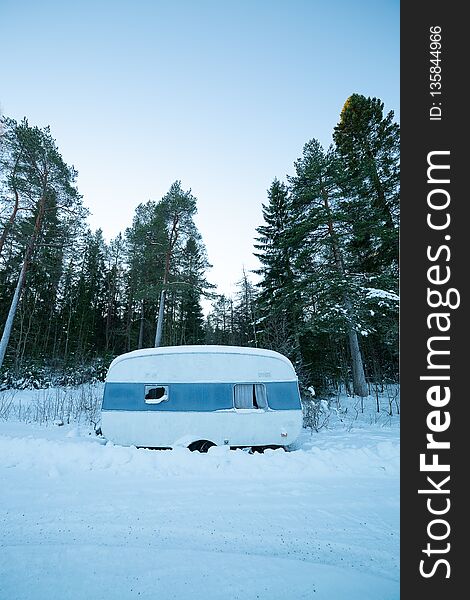 Rundown Camper Trailer in Winter with trees behind it