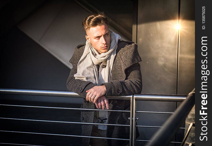 One handsome young man in urban setting in moden city, standing, wearing black coat and scarf in winter day. One handsome young man in urban setting in moden city, standing, wearing black coat and scarf in winter day