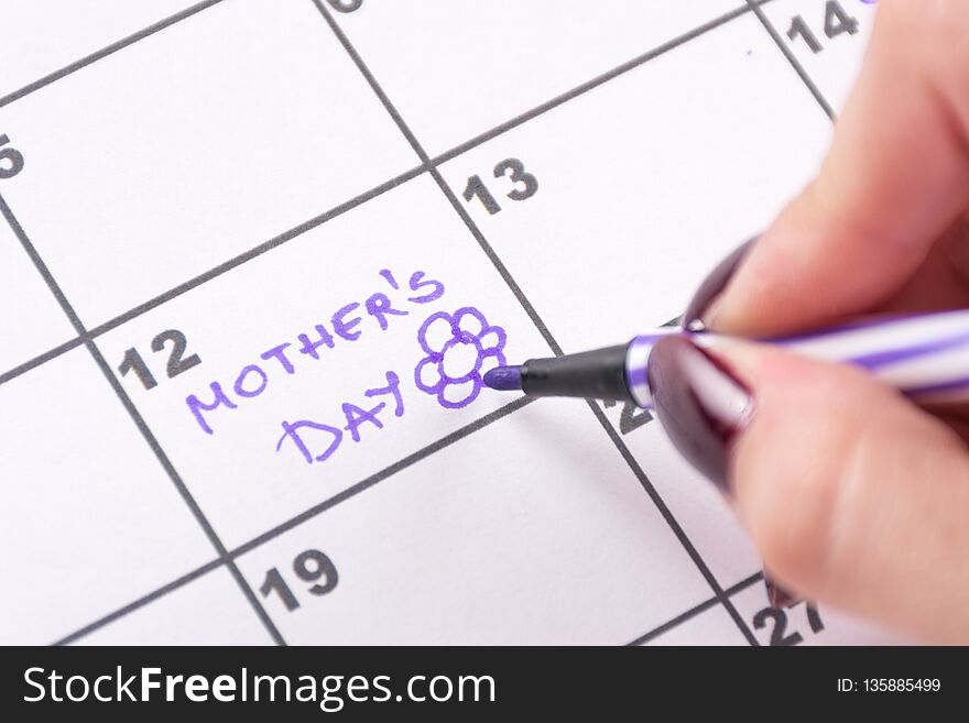 Woman hand writing Mothers Day and drawing flower with purple felt pen in calendar