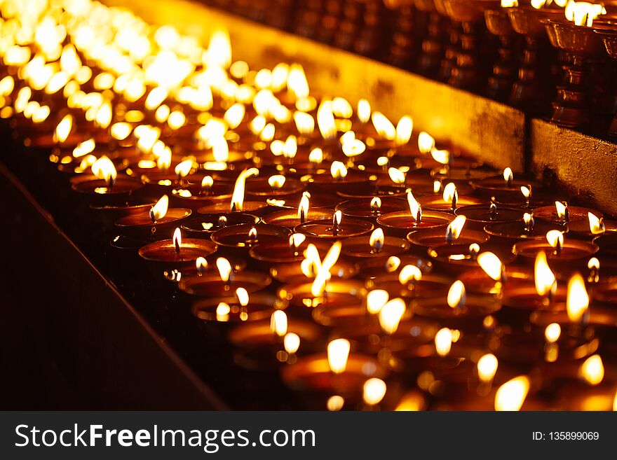 Many candle flames glowing in the dark with shallow depth of field