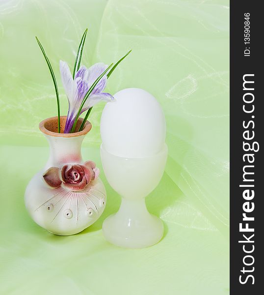 Egg in the  egg cup from onyx. Arrangement with crocus on the soft green fabric. Egg in the  egg cup from onyx. Arrangement with crocus on the soft green fabric.