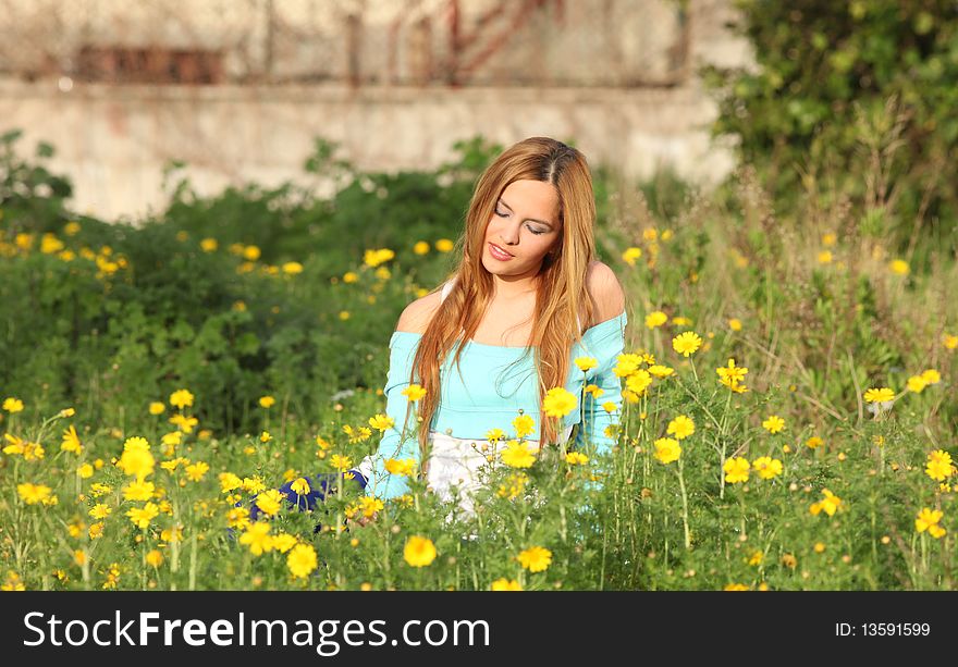 Beautiful young blonde woman sitting in blooming meadow in spring, smiling; shallow depth of field. Beautiful young blonde woman sitting in blooming meadow in spring, smiling; shallow depth of field
