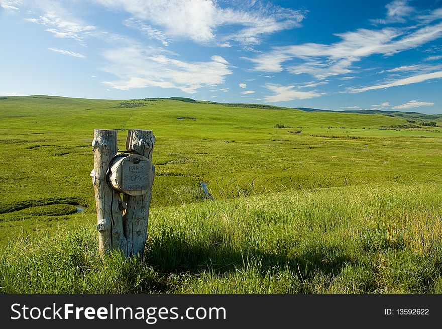 Weathered log mailbox with open grassy field and distant hills in BG. Sunny blue sky high white clouds. Name on mailbox is Bar S Ranch, Chataway. Weathered log mailbox with open grassy field and distant hills in BG. Sunny blue sky high white clouds. Name on mailbox is Bar S Ranch, Chataway.