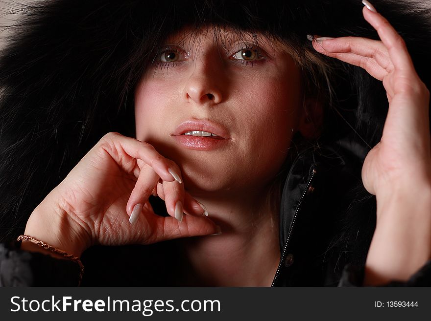 Young, nice looking woman covered with black fur hood by grey background. Young, nice looking woman covered with black fur hood by grey background