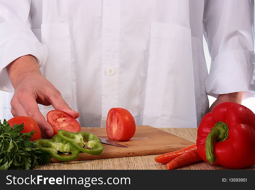 The cook holds in a hand a half of the cut tomato, in the foreground other vegetables.