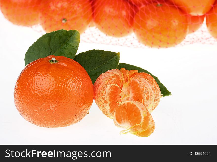 Ripe tangerine with a branch of a tree against a tangerines packed into a plastic grid.