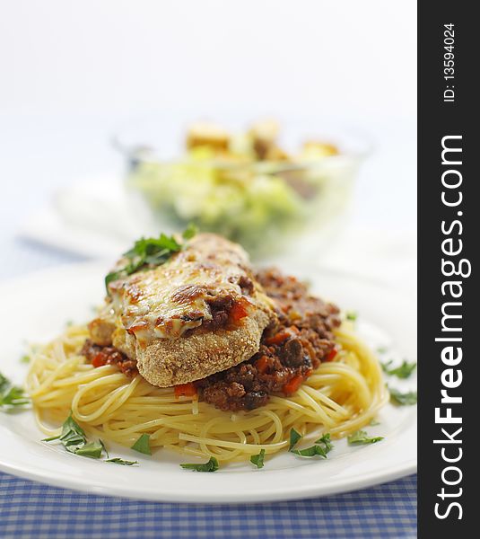 Chicken parmigiana meal on a spaghetti with tomato and meat sauce. Caesar salad in the background.Shallow depth of field. Chicken parmigiana meal on a spaghetti with tomato and meat sauce. Caesar salad in the background.Shallow depth of field.