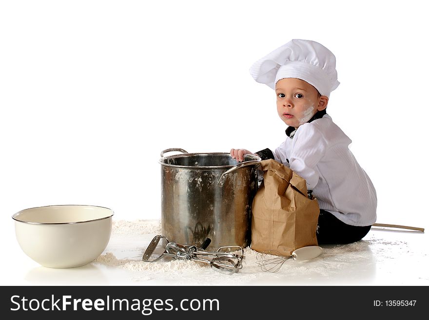 A toddler in a chef's outfit surrounded by cooking utensils and spilled flour. A toddler in a chef's outfit surrounded by cooking utensils and spilled flour.