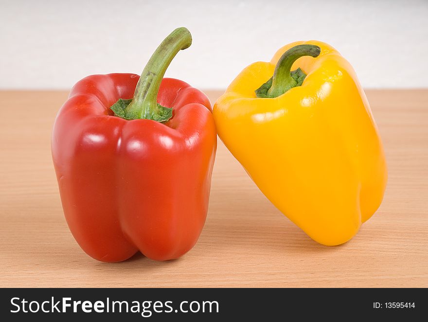 These are two red and yellow peppers are on the kitchen table. These are two red and yellow peppers are on the kitchen table