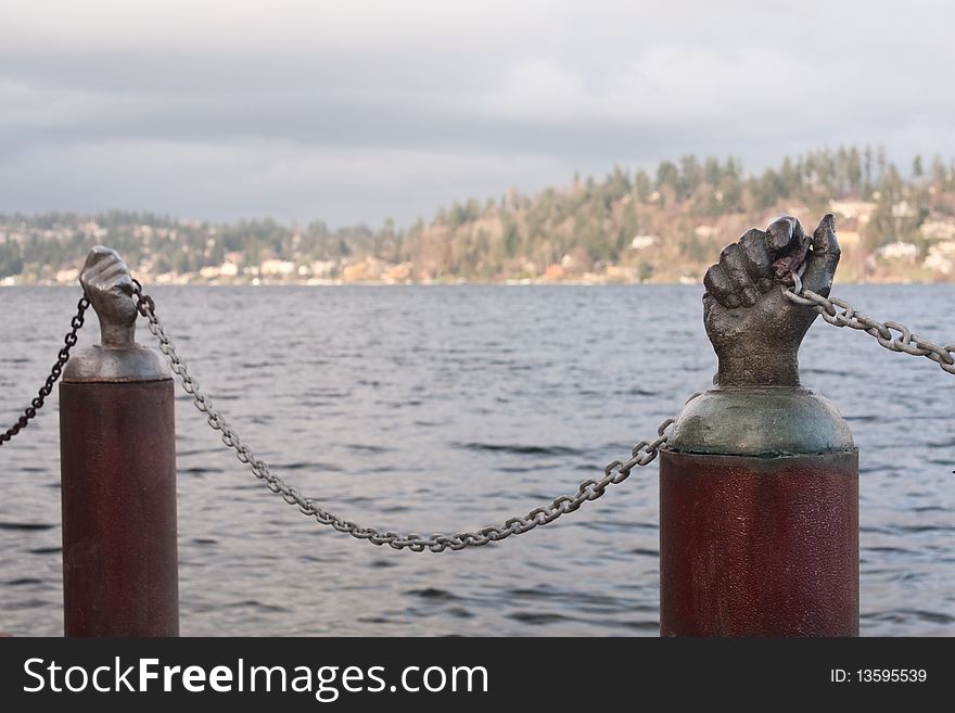 Bronze hands hold the chain that is the barrier to keep pedestrians from falling into the lake at a public park in Seattle, Washington. Bronze hands hold the chain that is the barrier to keep pedestrians from falling into the lake at a public park in Seattle, Washington.