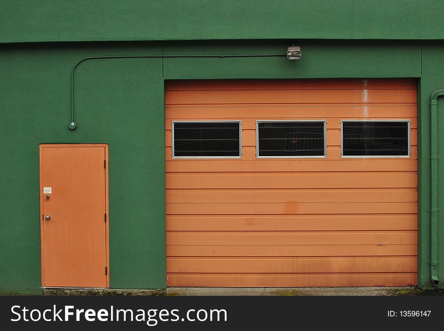 Small tan door next to a larger garage door set in a vivid green wall. Small tan door next to a larger garage door set in a vivid green wall.