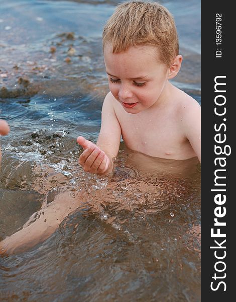 A young boy sits in a rock pool playing with the pebbles and rocks at Sodwana Bay, South Afica