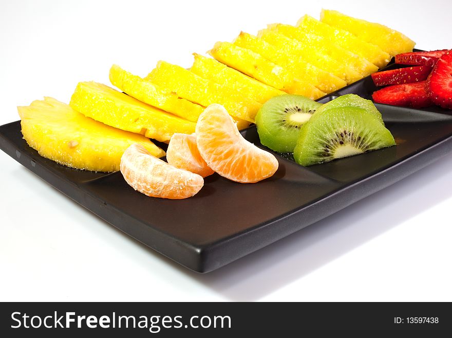 Sliced of ananas, kiwi, mandarin and strawberries on a black saucer. Sliced of ananas, kiwi, mandarin and strawberries on a black saucer