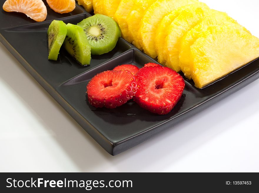 Sliced of ananas, kiwi, mandarin and strawberries on a black saucer. Sliced of ananas, kiwi, mandarin and strawberries on a black saucer