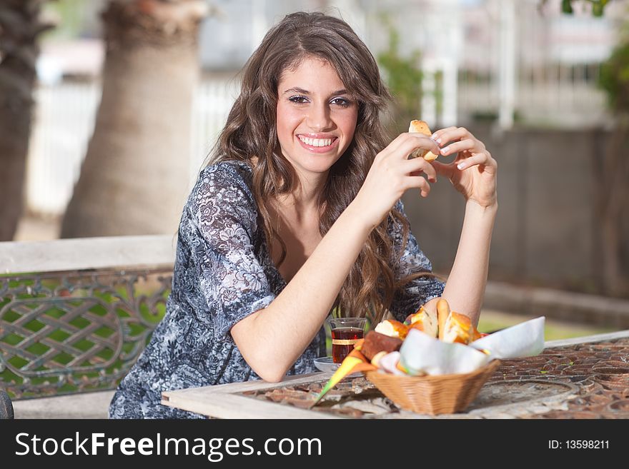 Beautiful young woman with great smile enjoying her breakfast outside, drinking tea, smiling to the camera; shallow depth of field. Beautiful young woman with great smile enjoying her breakfast outside, drinking tea, smiling to the camera; shallow depth of field