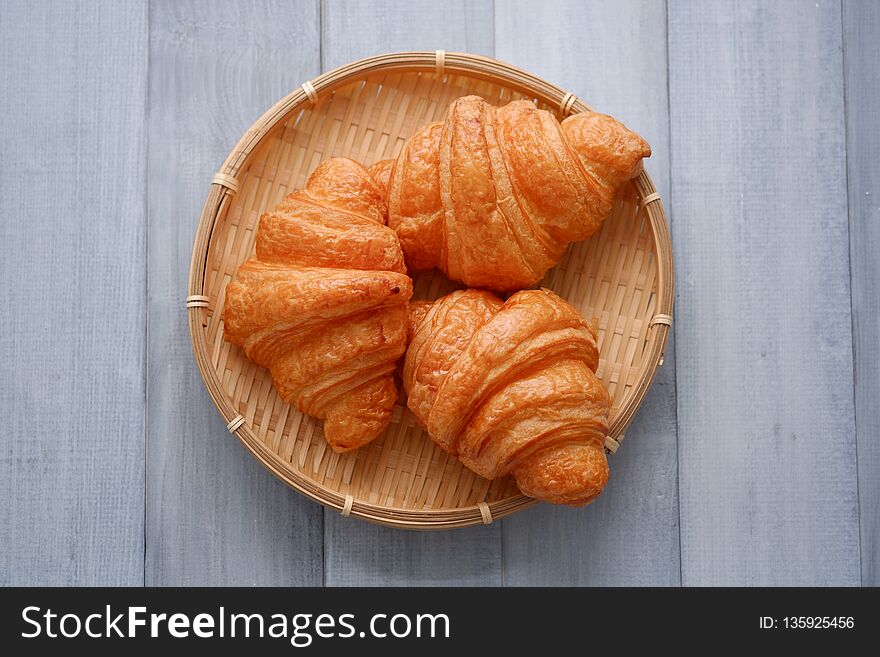 Fresh croissants in a basket weave on the white wood table.