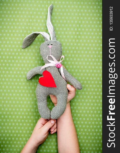 Valentine day. A child holds a rabbit with a red heart in his hand on a green polka dot background. Valentine`s Day. Heart pendant. Space for text. Red heart. Eighth of March. International Women`s Day.