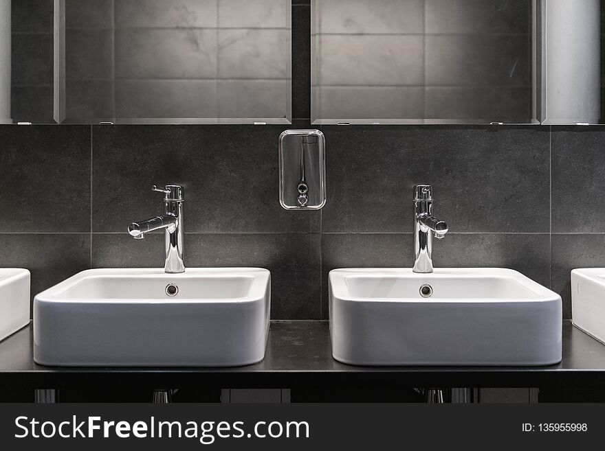 Clean new public toilet room empty. Two sinks and soap tank.