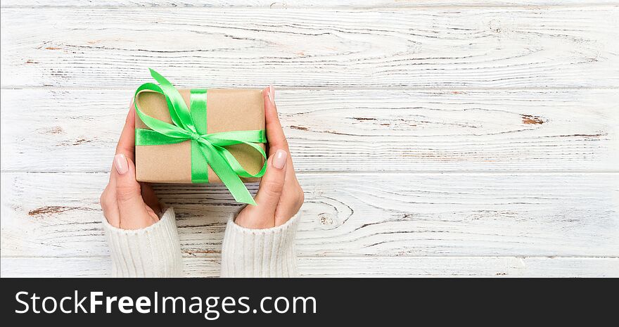 Woman hands give wrapped valentine or other holiday handmade present in paper with green ribbon. Present box, decoration of gift
