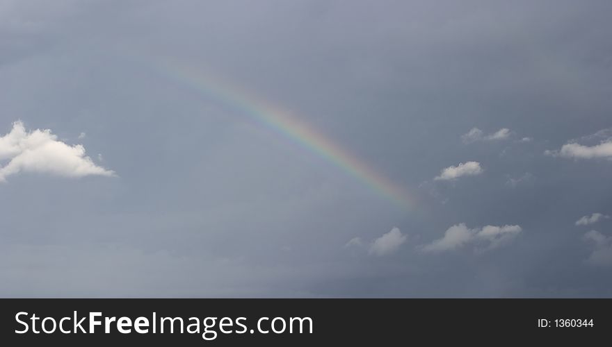 A rainbow in dark winter sky with white clouds. A rainbow in dark winter sky with white clouds