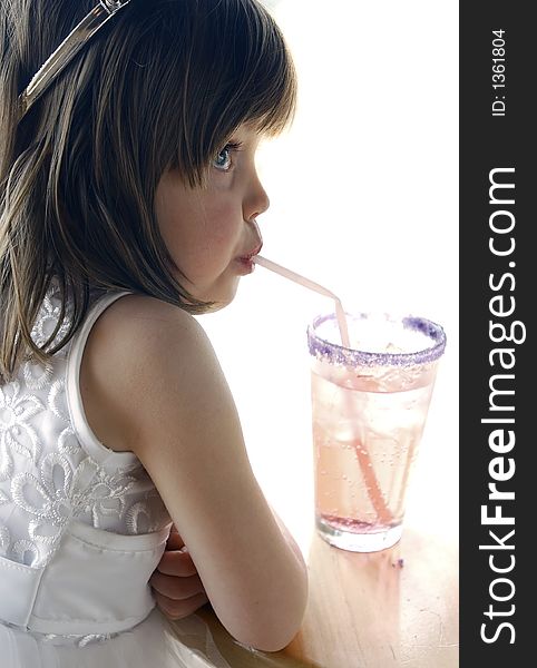 Young girl sitting at a table drinking a soda with a straw. Girl is wearing a princess costume and crown. Looking away from the camera. Young girl sitting at a table drinking a soda with a straw. Girl is wearing a princess costume and crown. Looking away from the camera.