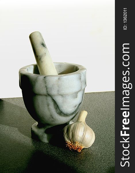 Pestle and Mortar with Garlic clove on a dark kitchen work surface with white background and room for copy/text