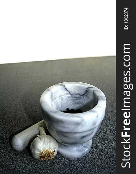 Pestle and Mortar with Garlic clove and black pepper corns, on a dark kitchen work surface with white background and room for copy/text. Pestle and Mortar with Garlic clove and black pepper corns, on a dark kitchen work surface with white background and room for copy/text