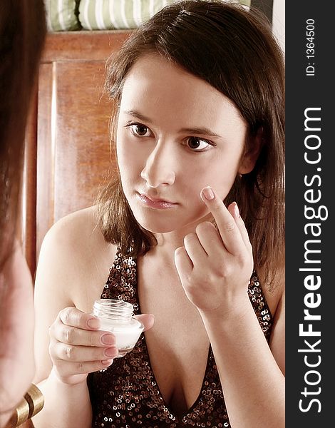 Auburn-haired girl, young woman putting cream in front of  a mirror