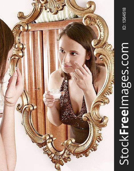 Auburn-haired girl, young woman putting cream in front of a mirror