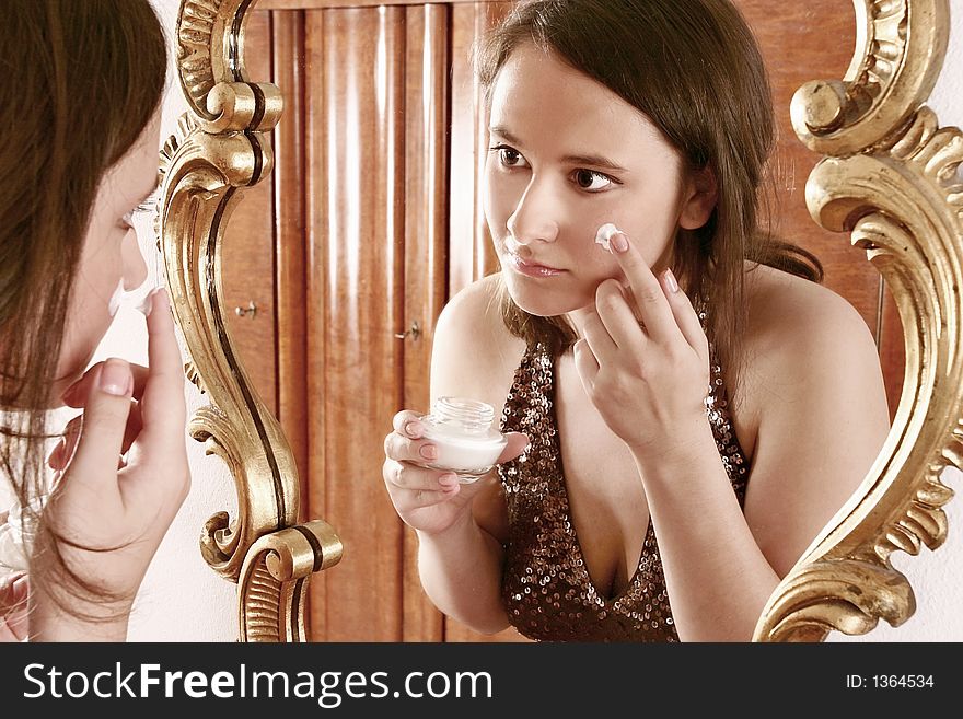 Auburn-haired girl, young woman putting cream in front of  a mirror